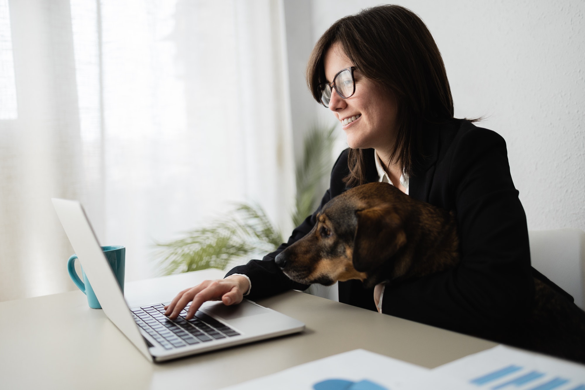 Happy business woman working in computer laptop with her dog at modern office - Focus on face