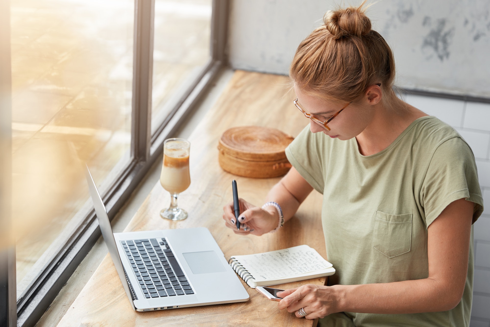 Une jeune femme devant son ordinateur avec un café en train d'écrire sur un bloc note, comme s'il réfléchissait à comment faire une stratégie pour un site internet